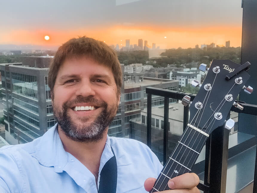 Ben Hammond selfie holding guitar with a Denver sunset glowing behind